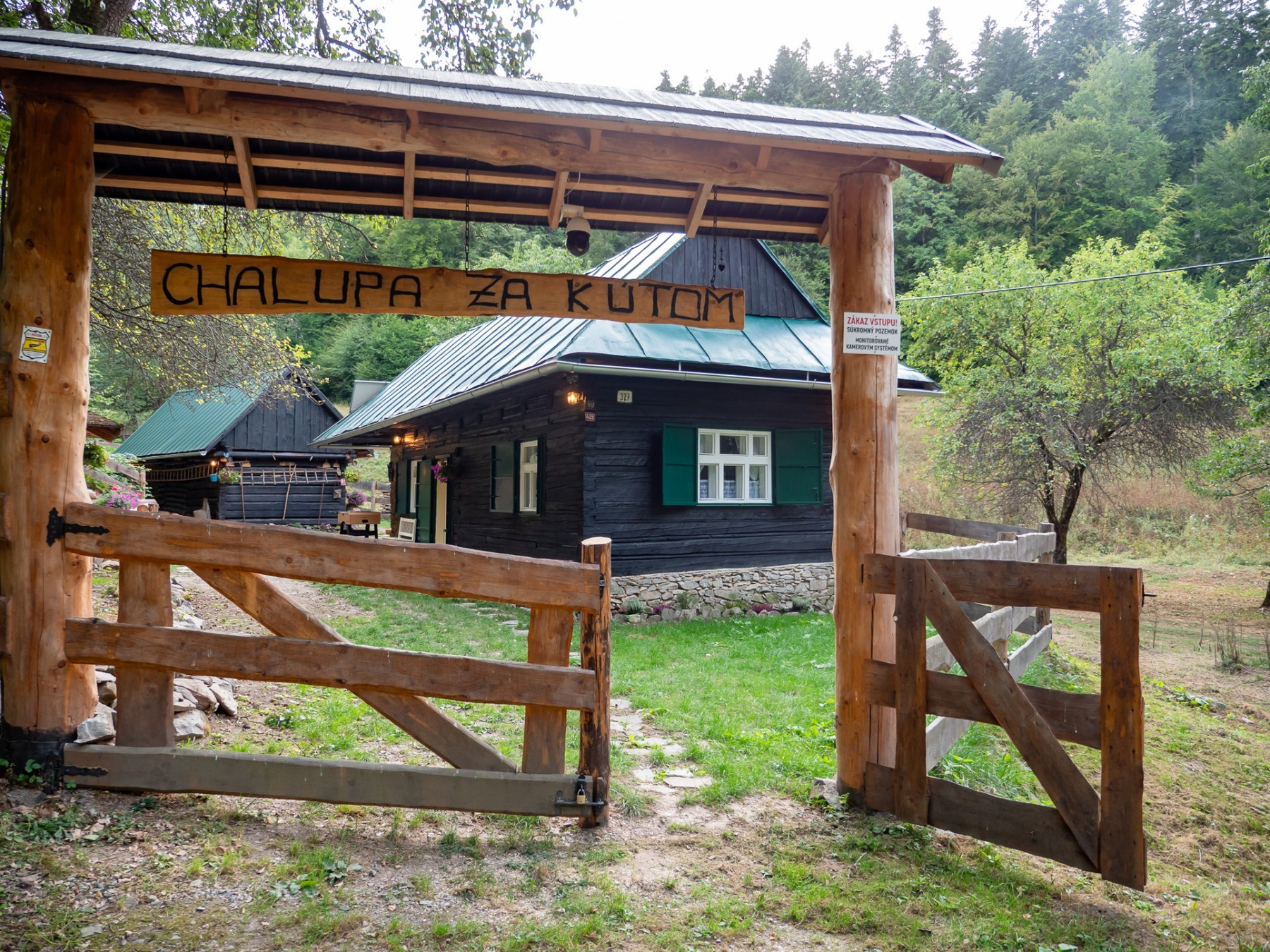 Vstup do areálu Chalupy Za Kútom s dřevěnou bránou a chatou v lese